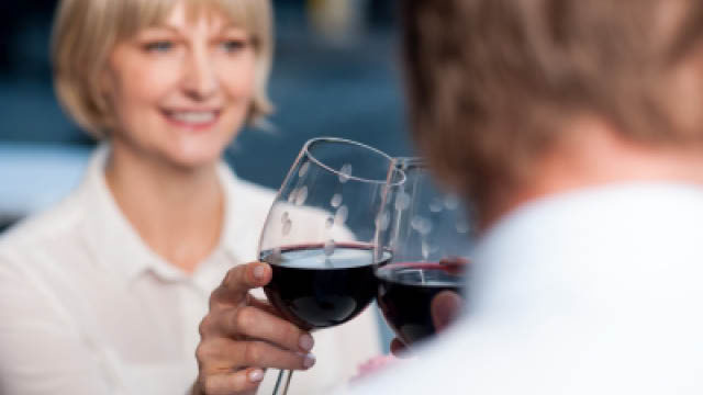 Attractive couple raises a glass of red wine in cafe.