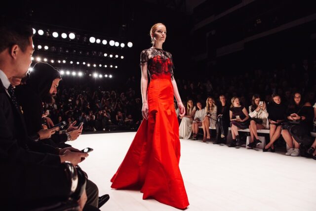 Women walking down the a catwalk in a red evening dress