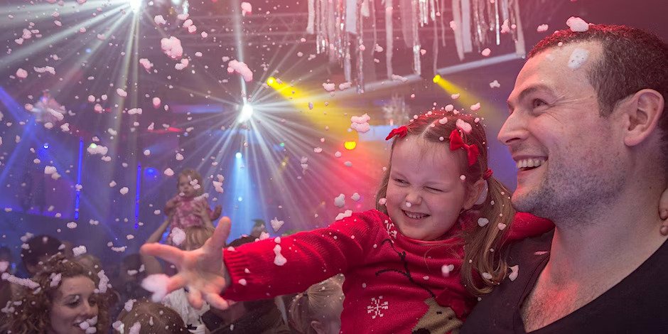Parent holding a little girl at a party with foam, lights and sparkles