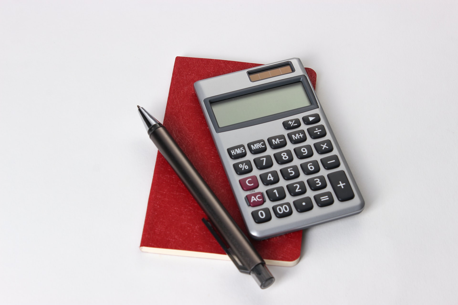 black and silver calculator beside a black pen and red notepad