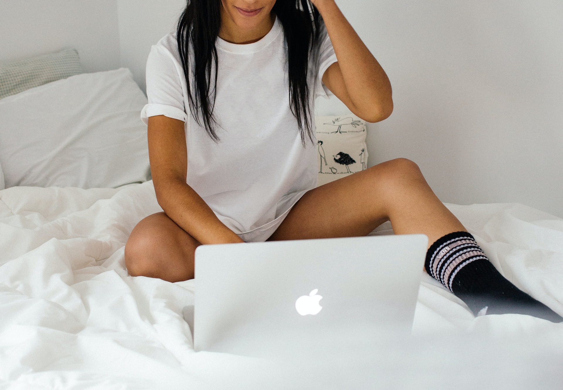 Women wearing a white t-shirt, sitting on a bed, using an imac