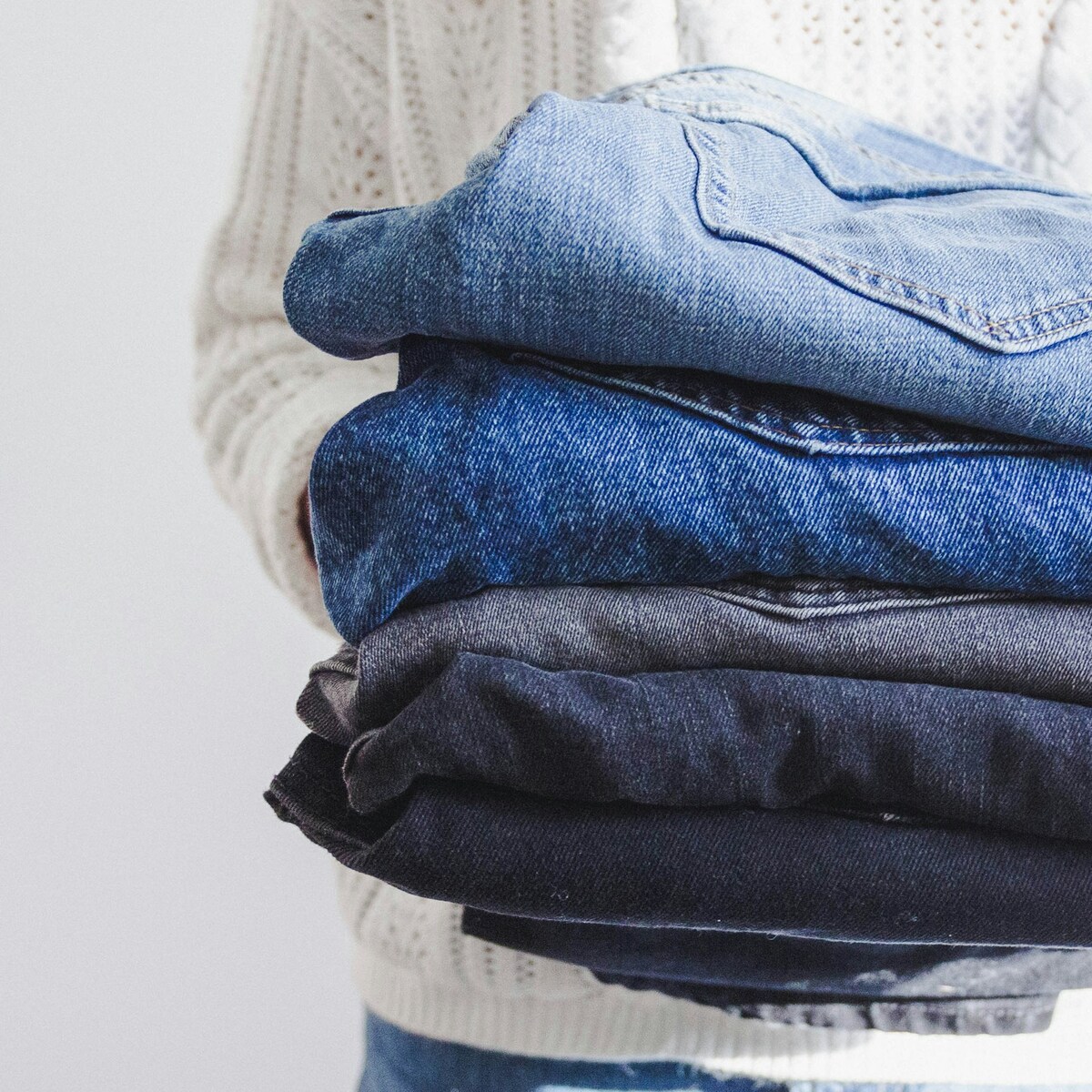 A person holding a pile of folded denim