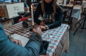 From Screen to Reality: How Pop Culture Shapes Our Views on Love and Dating Man and women holding hands over a table with a glass of red wine