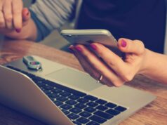 The Role of Bulk SMS Marketing in the Entertainment Industry A woman holding her phone and reading their SMS messages while using a laptop