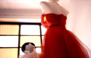A mannequin displays a vibrant red dress near a window.