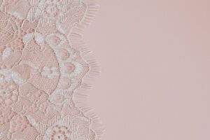 Delicate white lace fabric on a soft pink background.