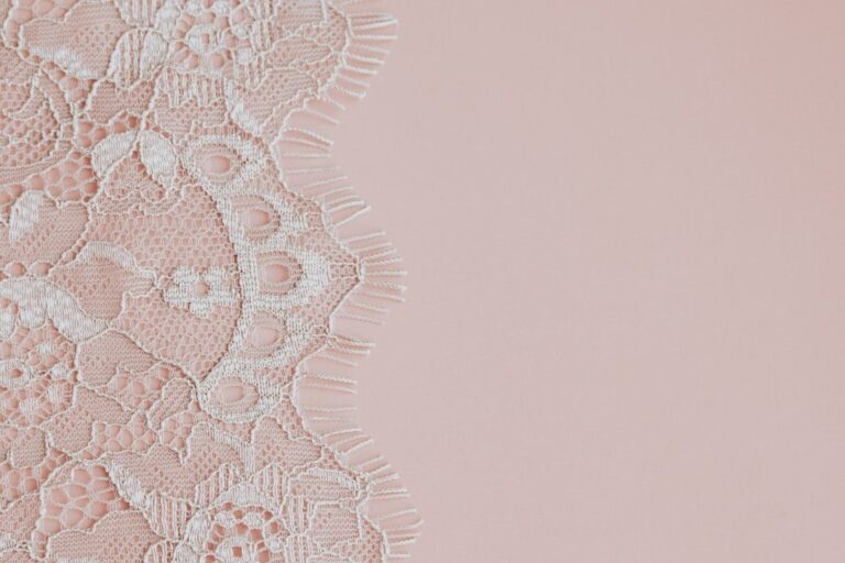Delicate white lace fabric on a soft pink background.