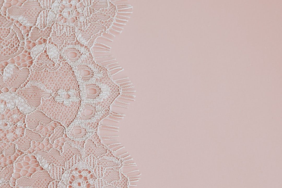 Delicate white lace fabric on a soft pink background.