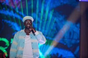Man in hat and glasses holding microphone on stage.