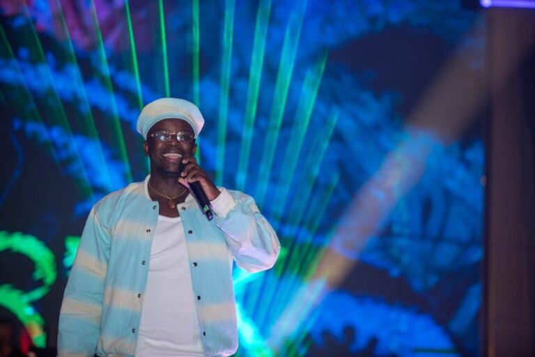 Man in hat and glasses holding microphone on stage.