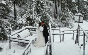 A bride and groom standing on a bridge in the snow