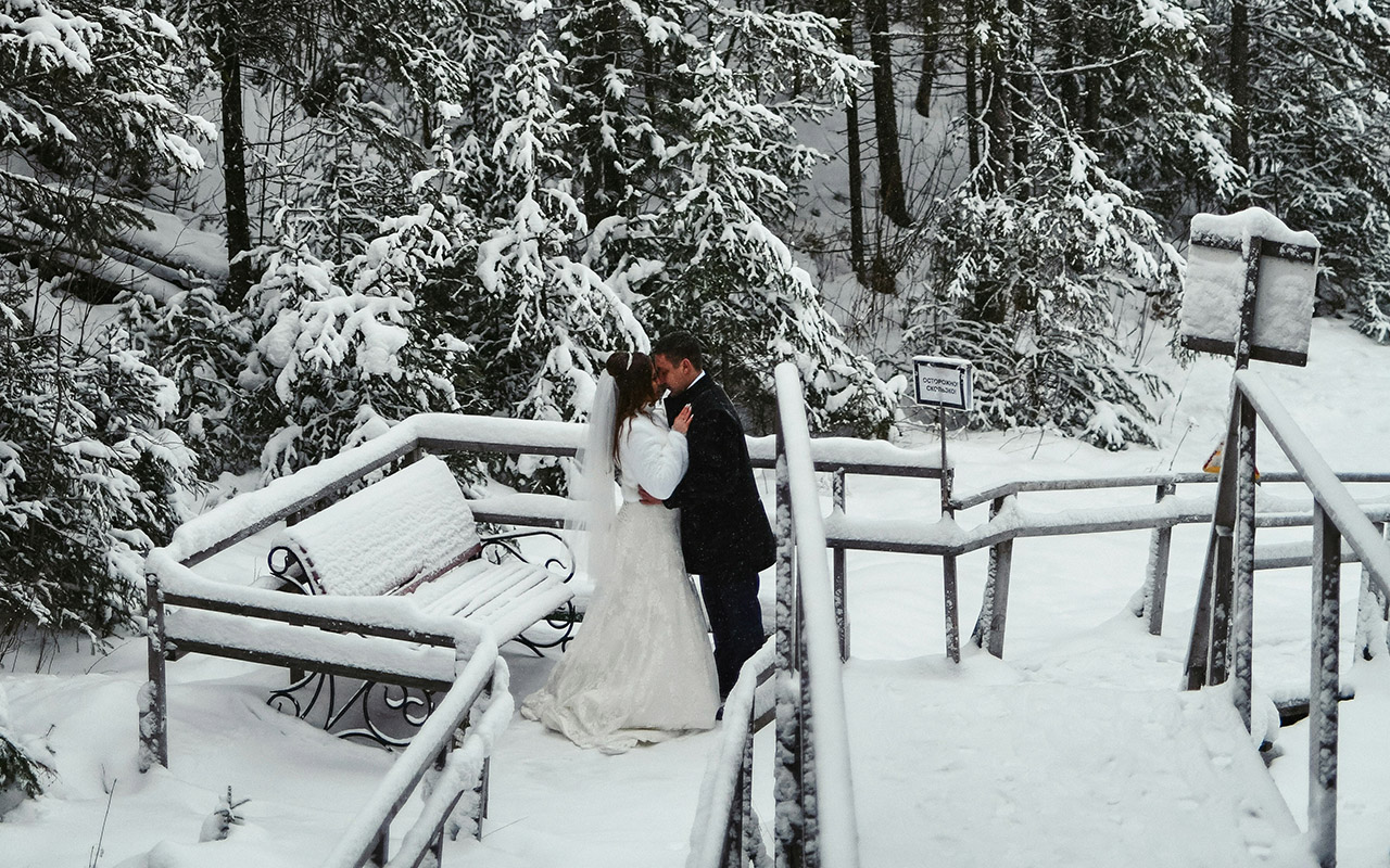 A bride and groom standing on a bridge in the snow