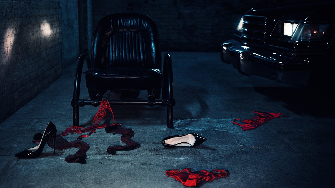 Red Agent Provocateur knickers, stockings and heels scattered on a concrete floor beside a chair