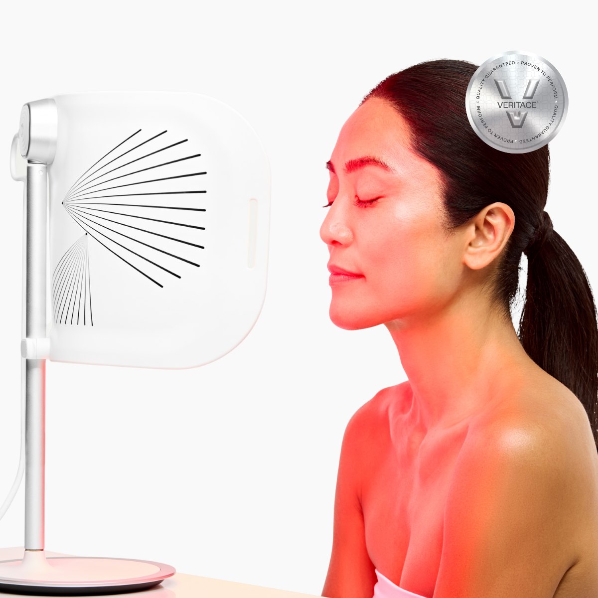 Woman sitting beside the CurrentBody Skin LED Light Therapy Panel, her face lit red
