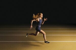Keely Hodgkinson sprinting on a gold-lit track in her navy Nike signature collection